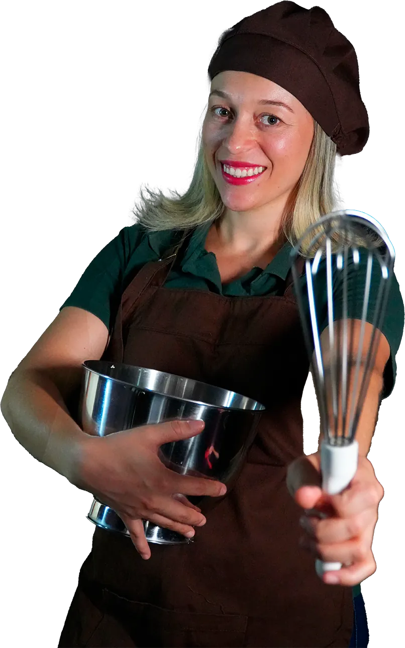 Dani, fundadora da Amor Quentinho, sorrindo de touca e avental, abraçando uma tigela de inox e apontando um batedor